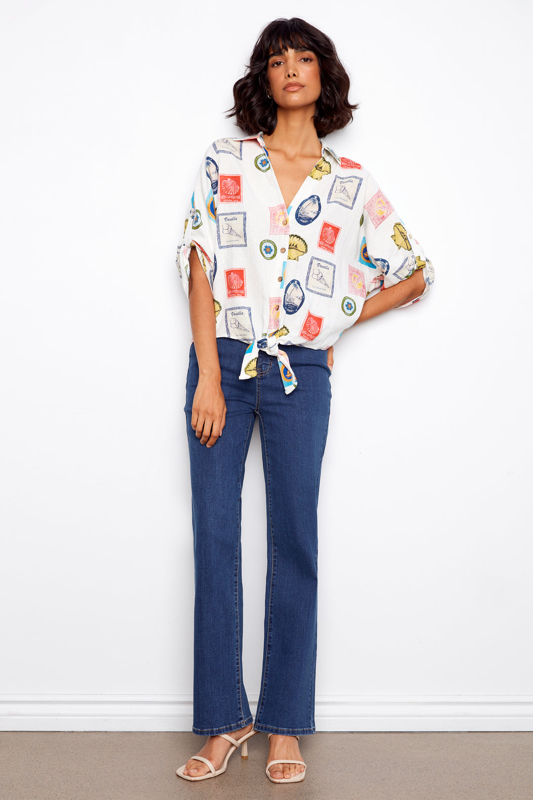 Woman wearing a colorful patterned blouse and blue jeans against a white background