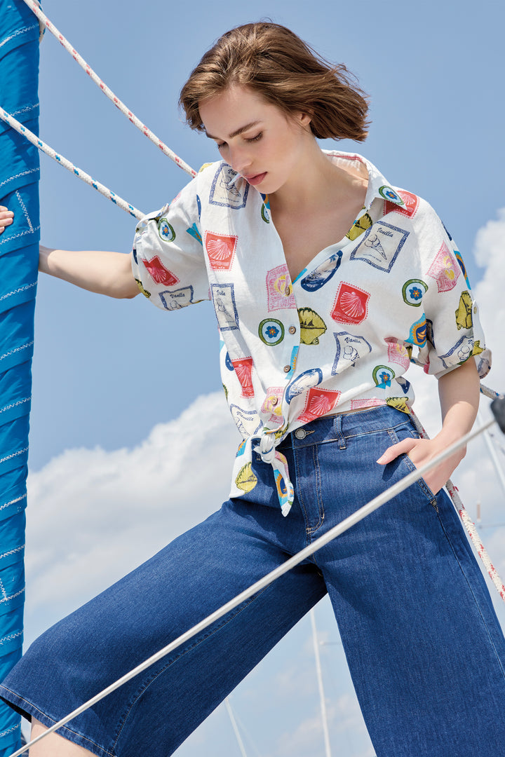 Woman wearing a colorful patterned blouse and blue jeans on a boat against a blue sky.
