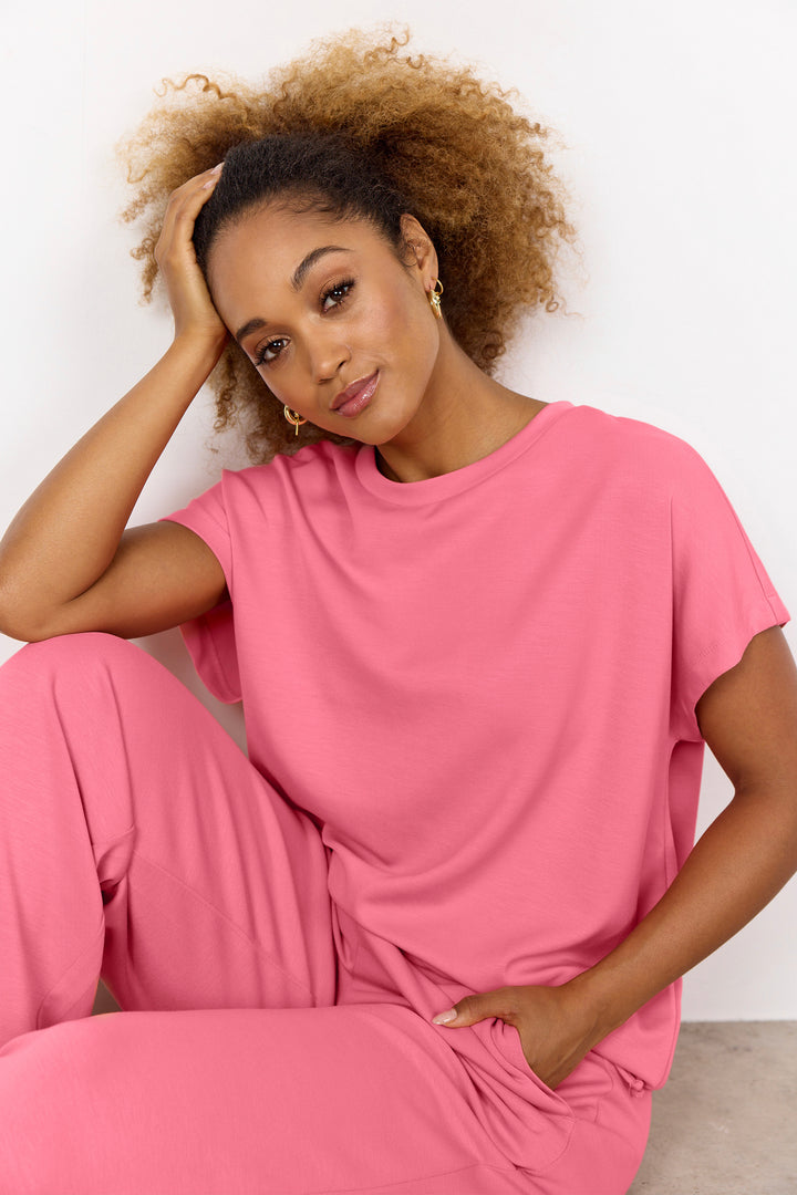 Woman wearing a pink top with tie waist sitting against a white background