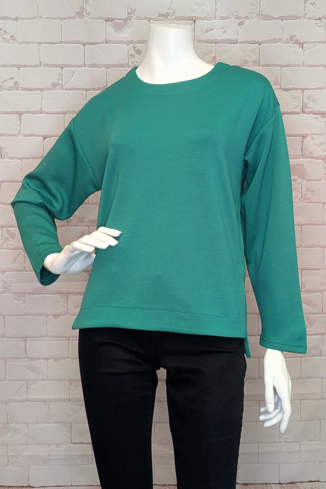 Green long-sleeve sweater top on a mannequin against a brick wall background