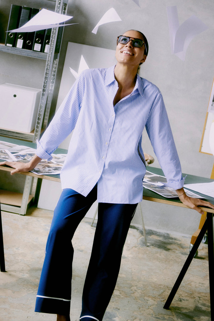 Person wearing a blue and white striped shirt and dark pants in an office setting.