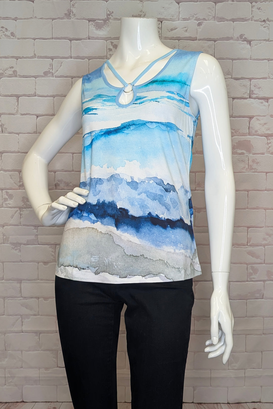 Mannequin wearing a sleeveless blue and gray patterned tank top against a brick wall.