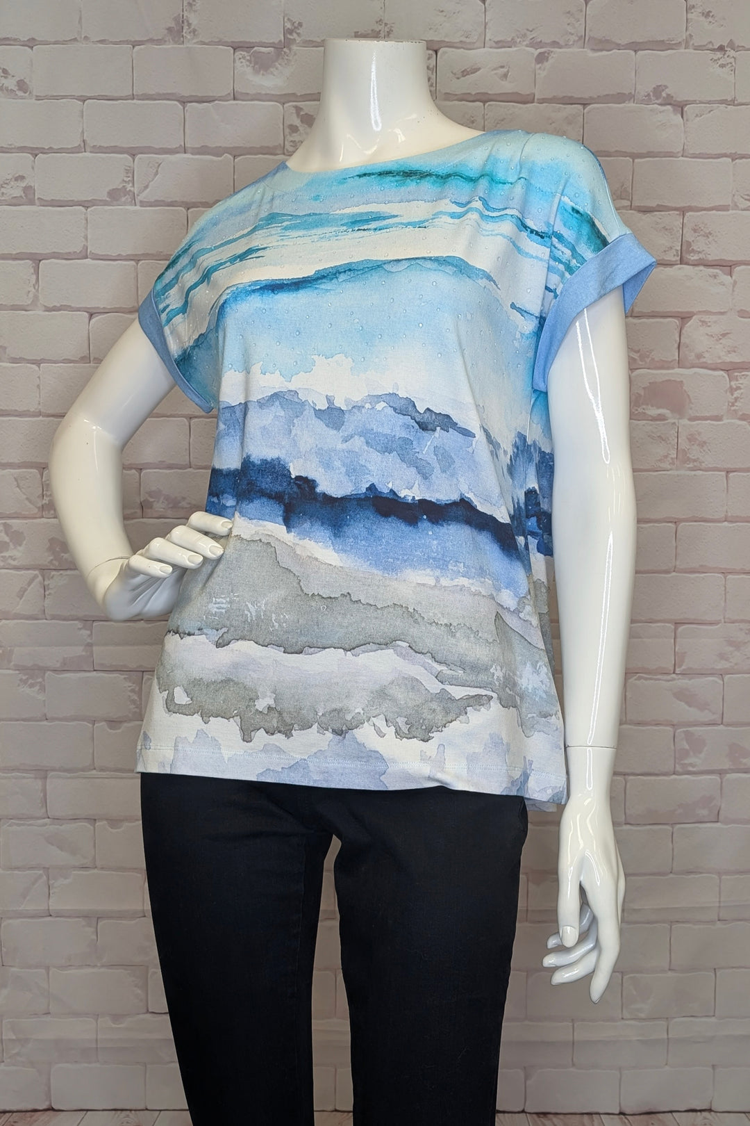 Mannequin wearing a blue and white abstract patterned top against a brick wall.