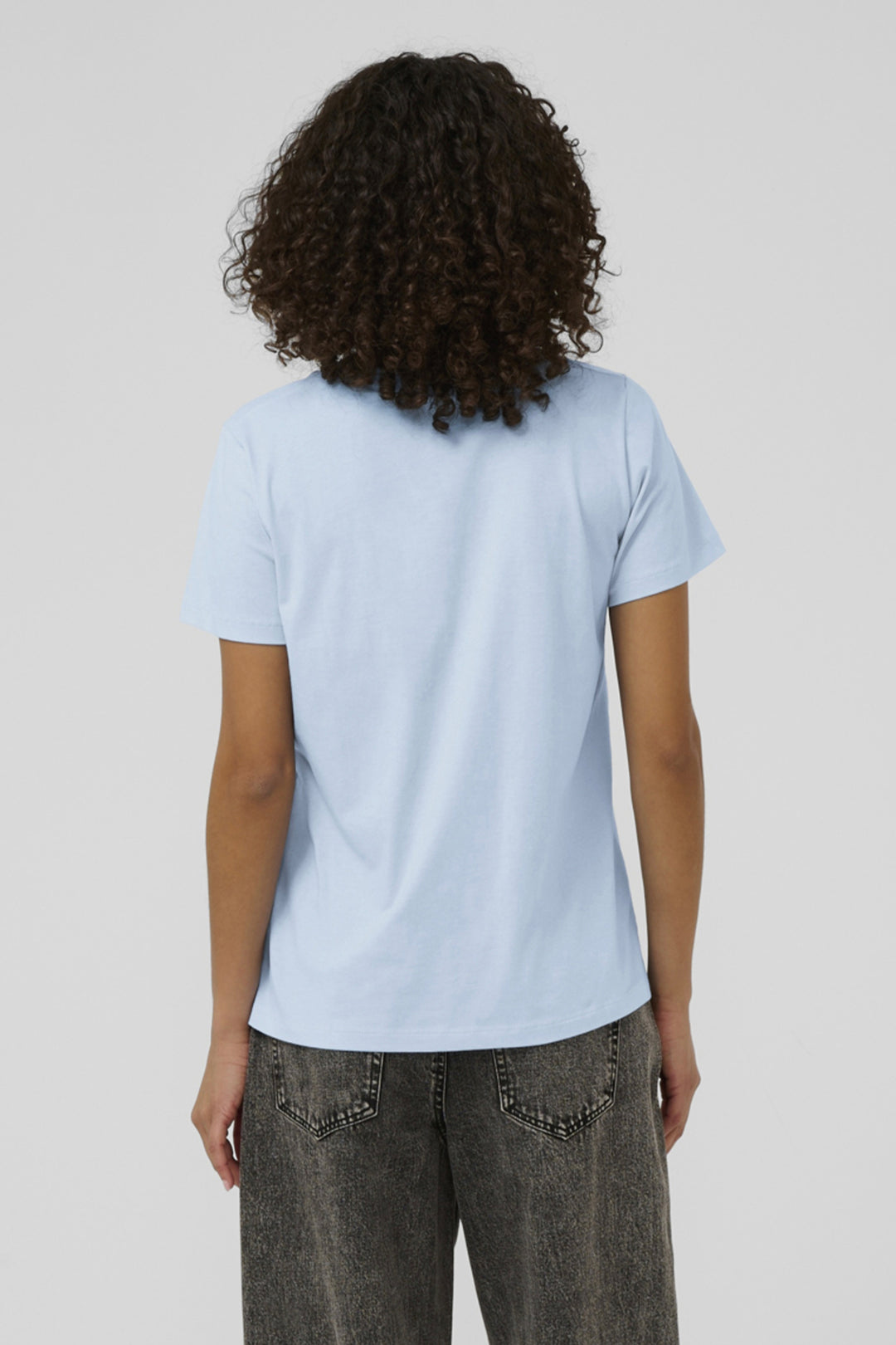 Person wearing a light blue t-shirt and dark jeans on a plain background