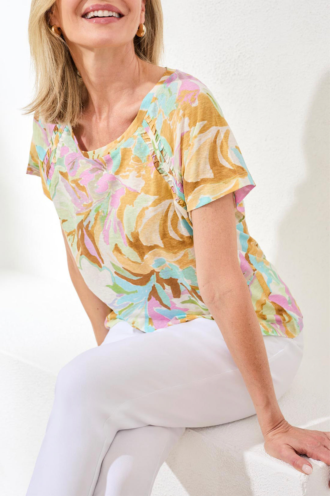 Woman wearing a colorful floral blouse and white pants on a white background