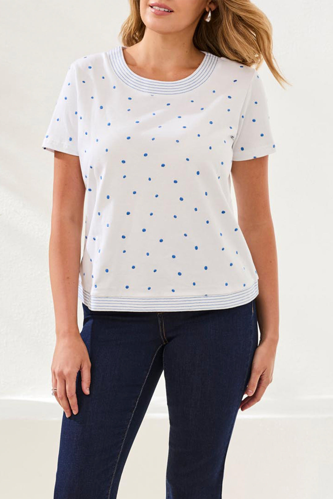 Woman wearing a white t-shirt with blue polka dots and dark jeans on a plain background