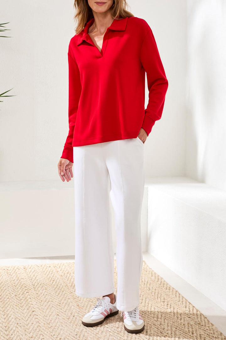 Person wearing a red blouse and white pants in a minimal indoor setting