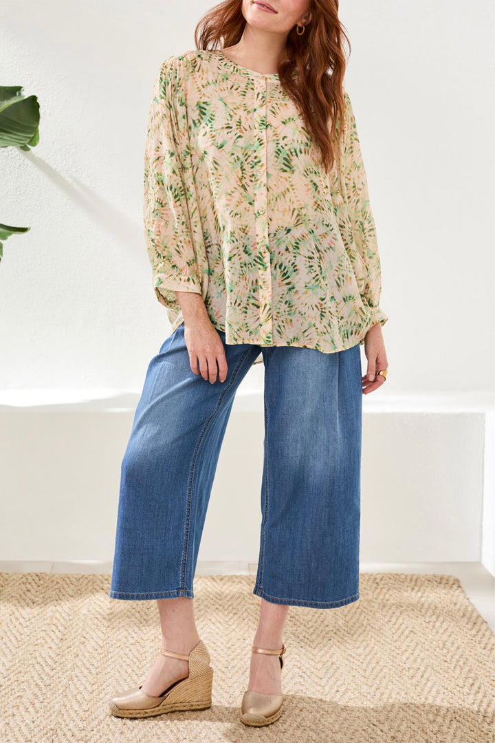 Woman wearing a floral blouse and blue jeans standing indoors.