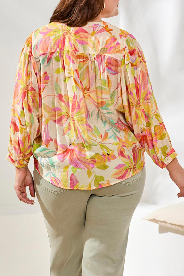 Person wearing a colorful floral blouse with beige pants on a white background