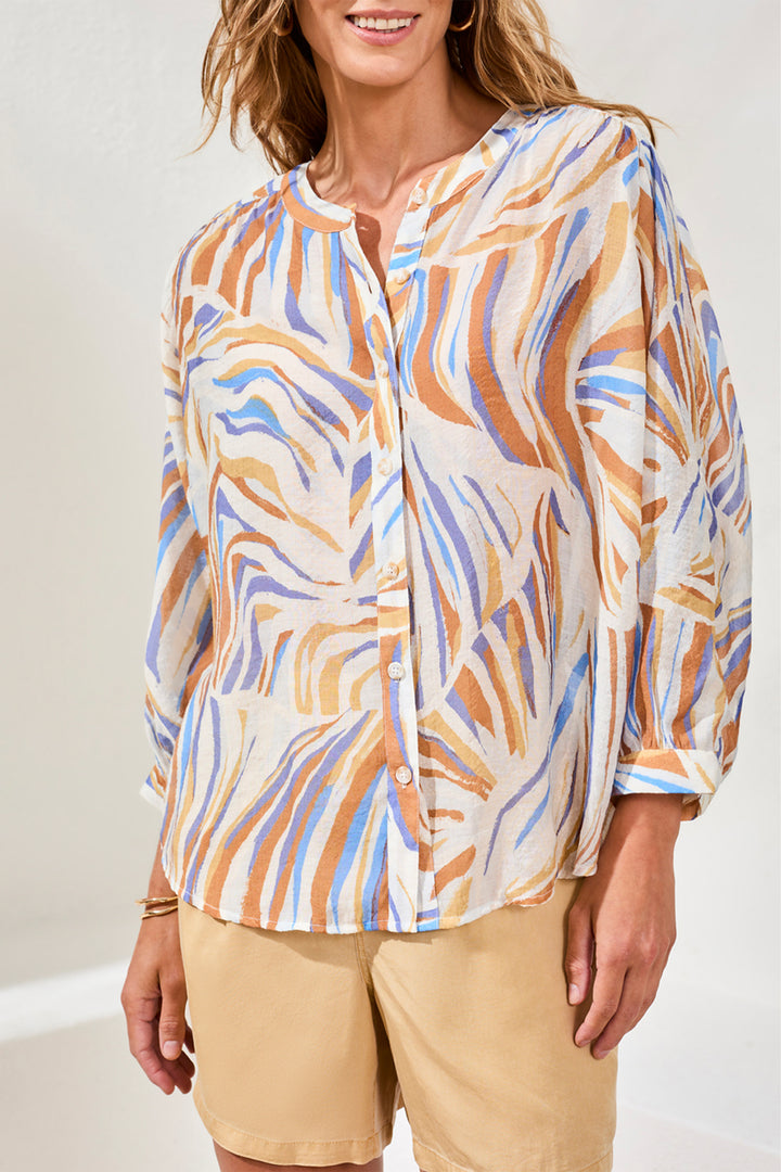 Woman wearing a patterned button blouse with long sleeves and beige shorts on a white background