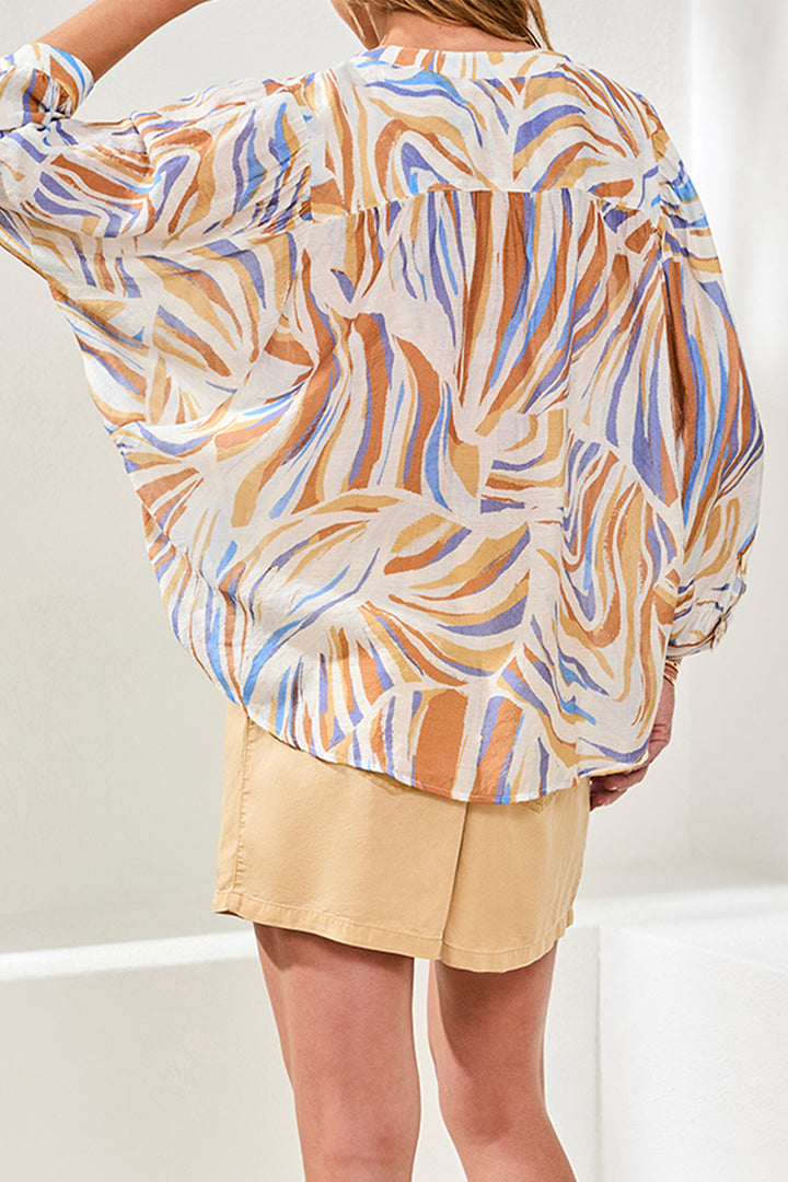 Person wearing a patterned blouse and beige skirt on a plain background