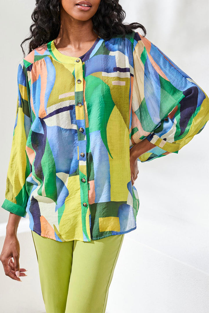 Woman wearing a colorful patterned button top and green pants on a white background