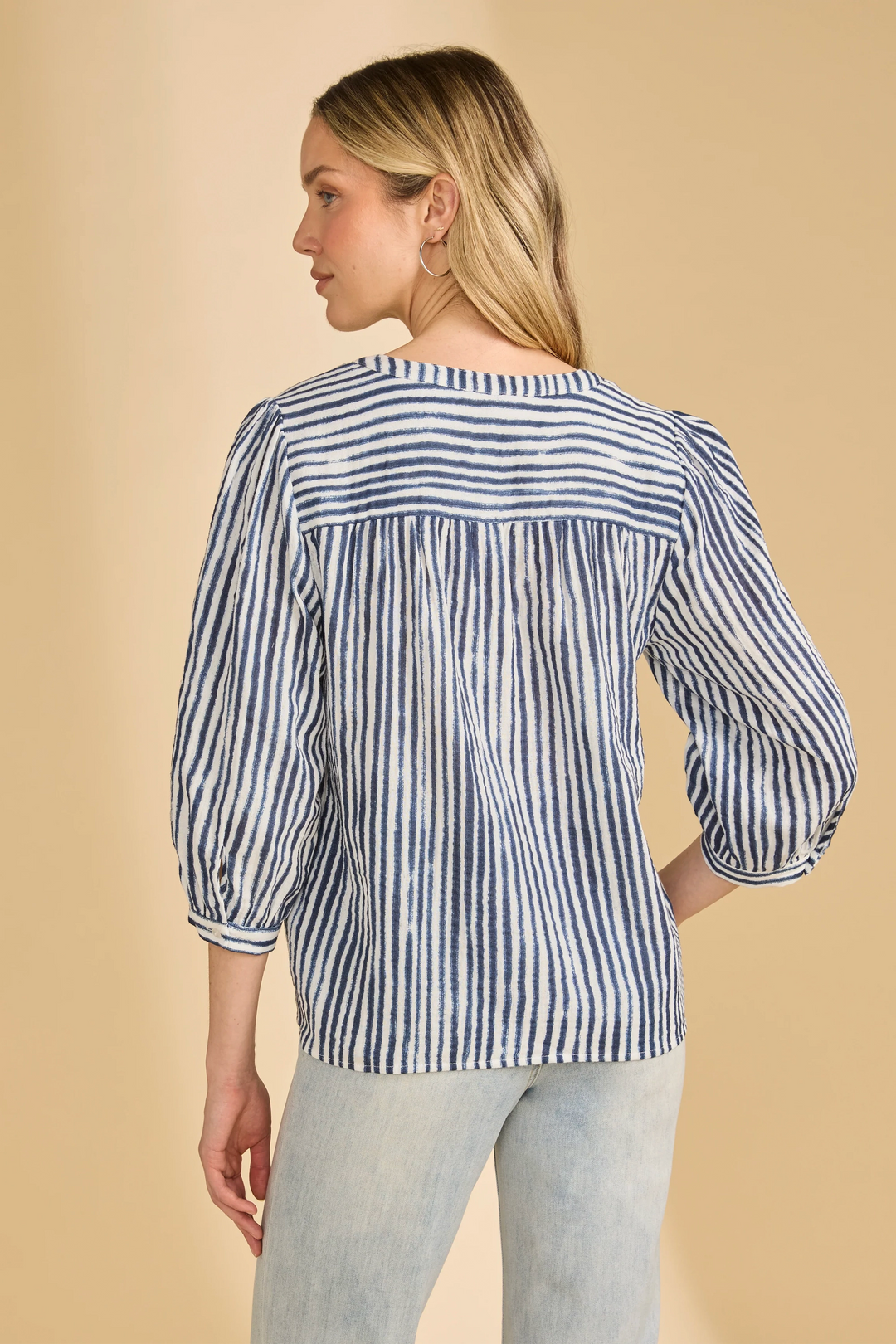 Woman wearing a blue and white striped blouse against a beige background