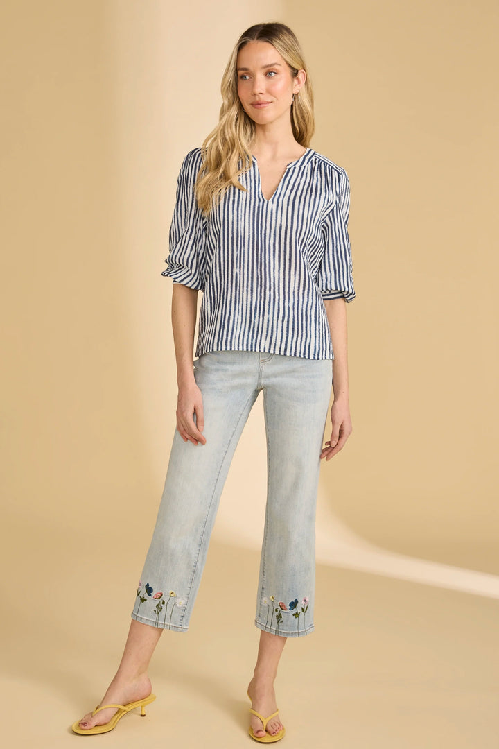 Woman wearing a blue and white striped shirt and light blue jeans with floral embroidery on a beige background