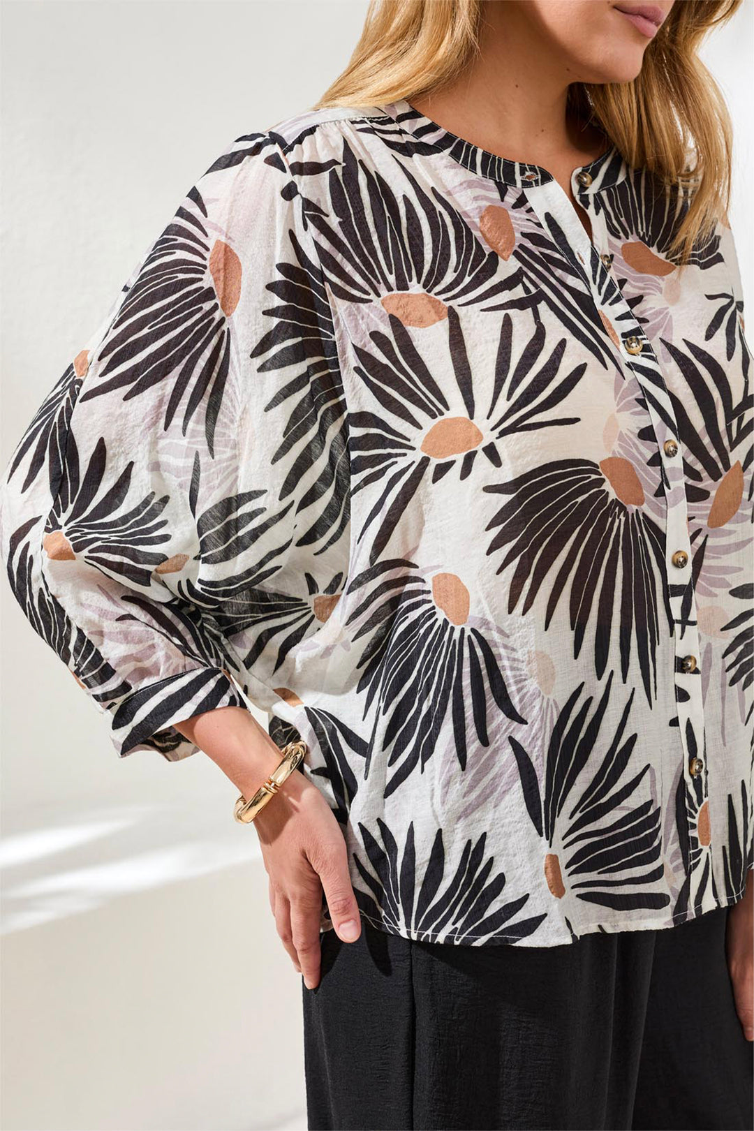 Woman wearing a black and white floral blouse with long loose sleeves.