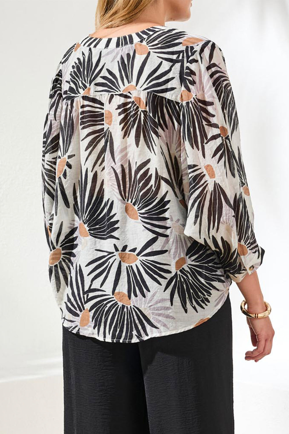 Woman wearing a patterned blouse with black and white design on a plain background