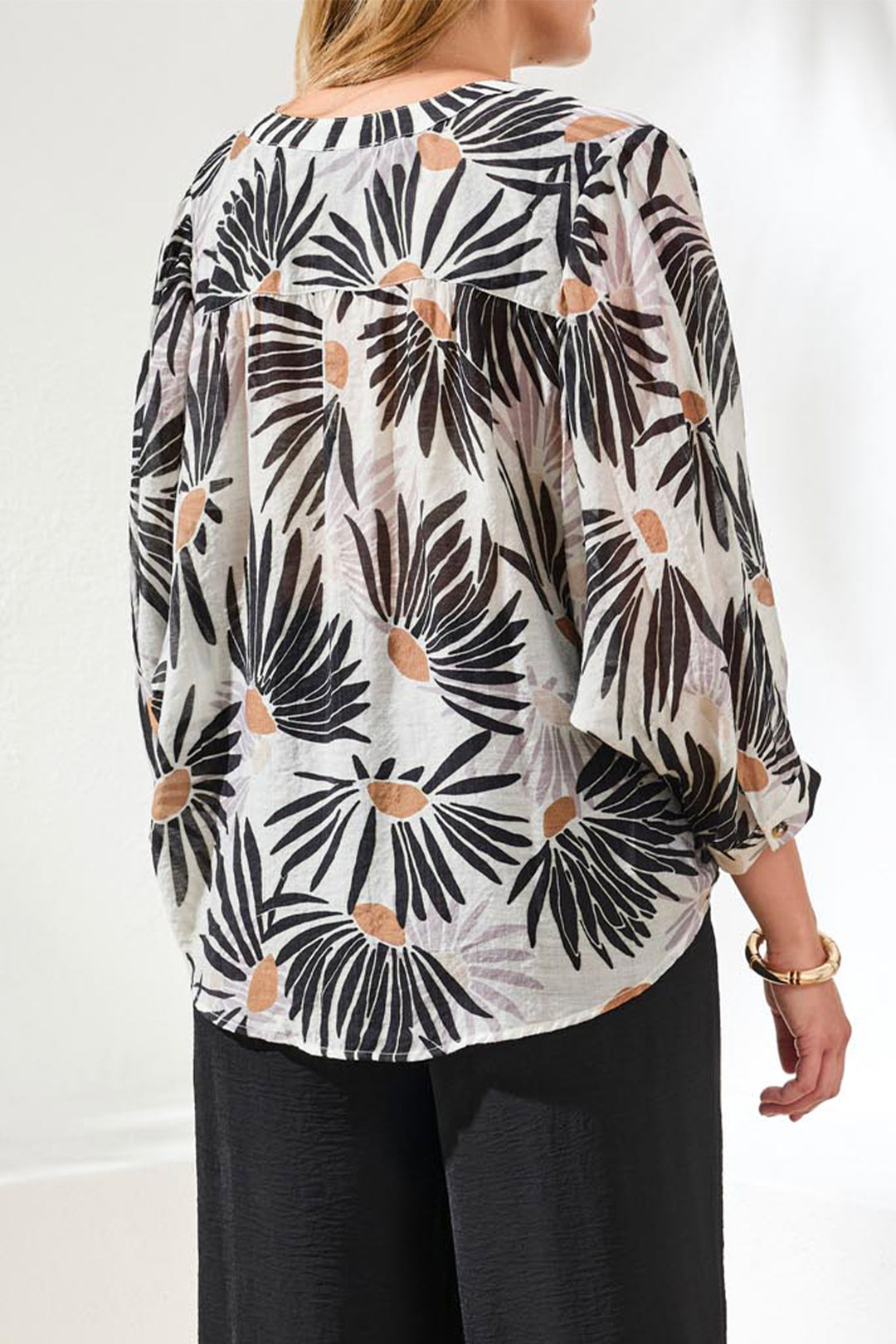 Woman wearing a patterned blouse with black and white design on a plain background