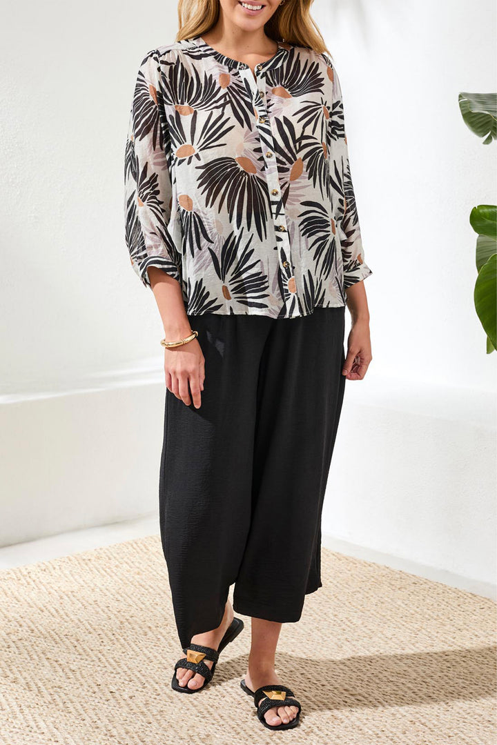 Woman wearing a patterned blouse and black pants indoors.