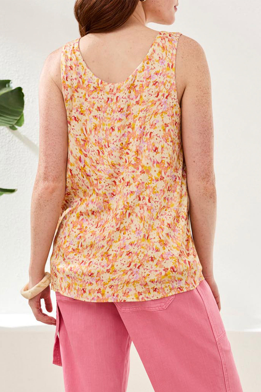 Person wearing a floral sleeveless top and pink pants on a white background