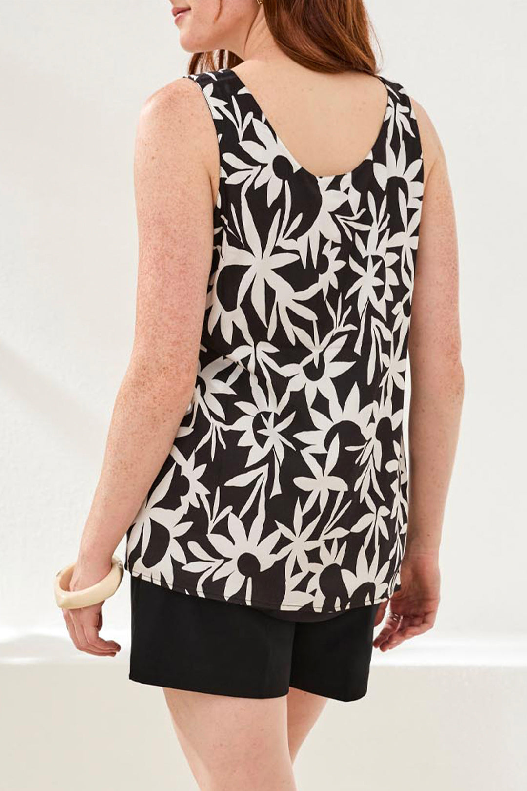 Person wearing a black and white floral sleeveless top with black shorts on a white background