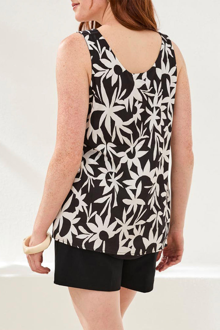 Person wearing a black and white floral sleeveless top with black shorts on a white background
