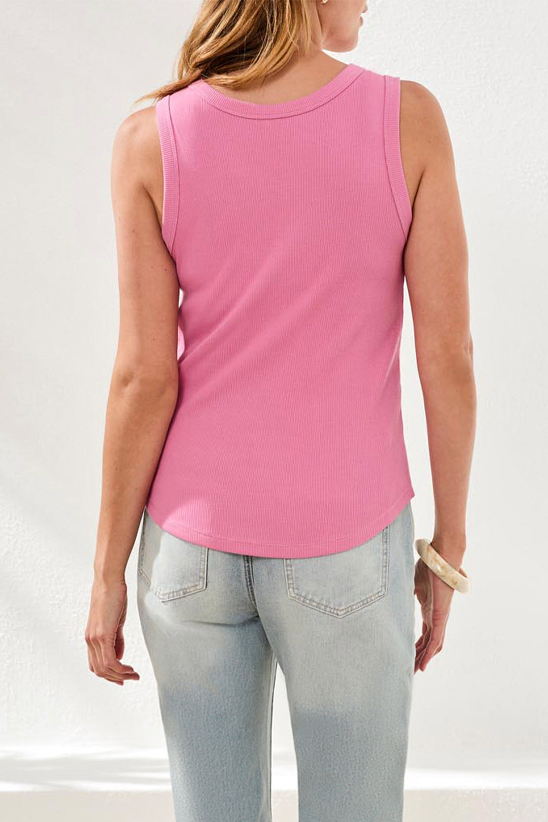 Person wearing a pink sleeveless top and light blue jeans against a white background