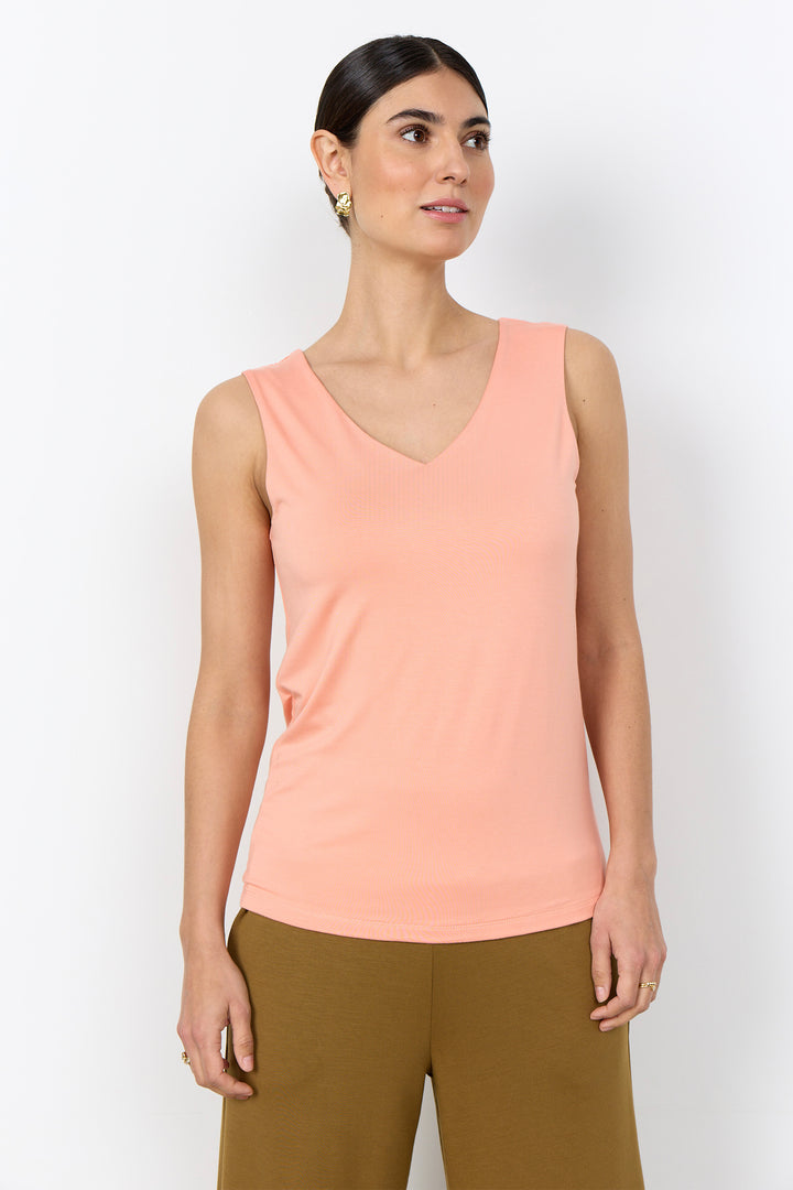 Woman wearing a light pink coloured tank top with wide straps on a white background. 