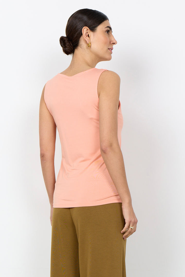 Woman wearing a light pink coloured tank top with wide straps on a white background. 