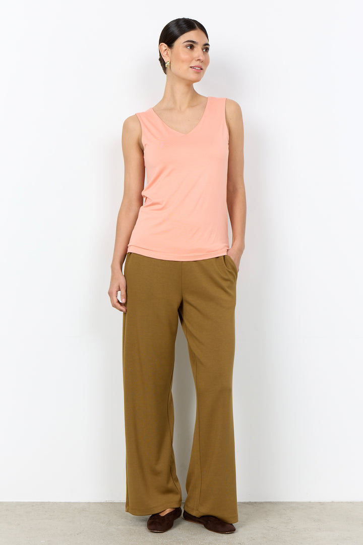 Woman wearing a light pink coloured tank top with wide straps on a white background. 
