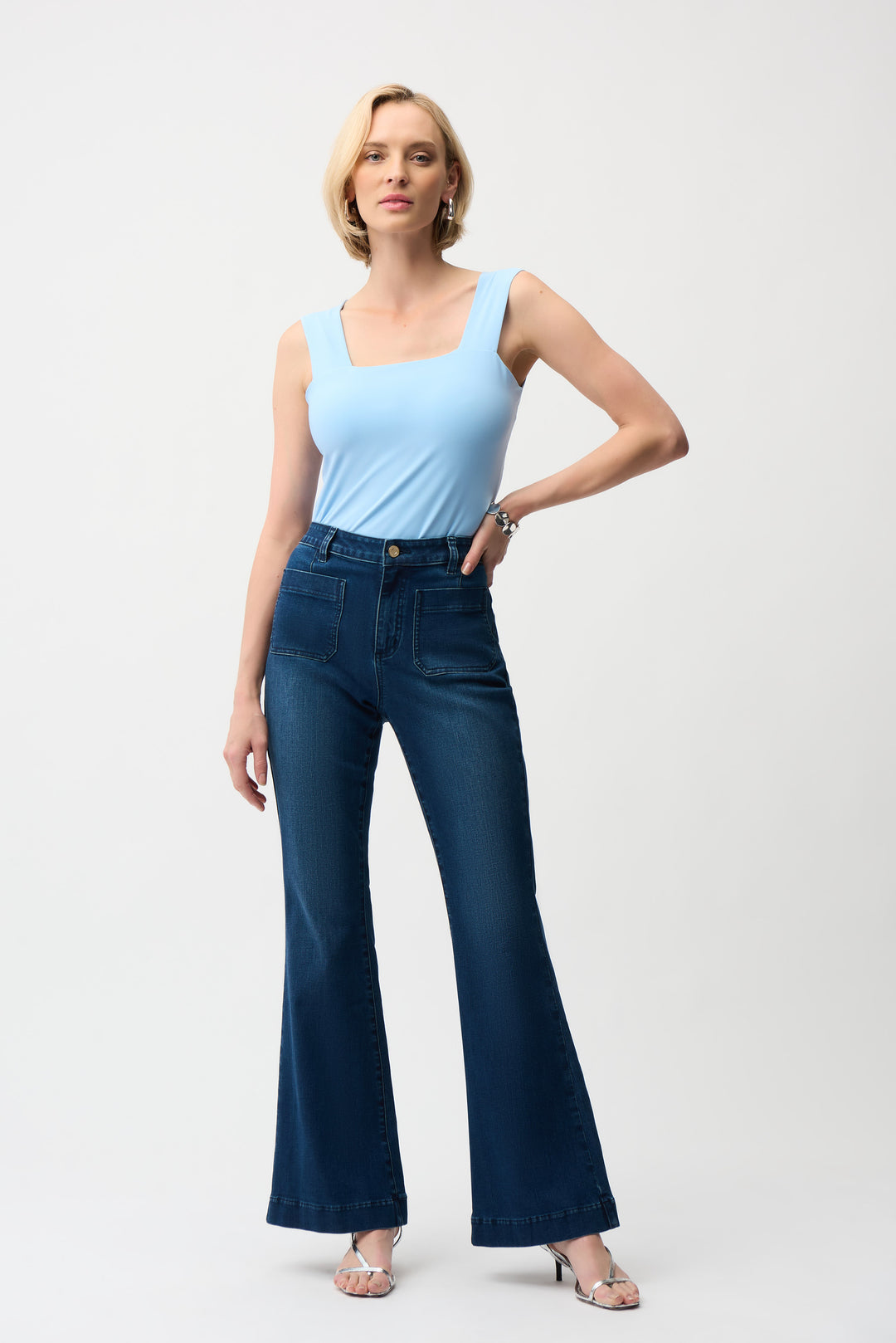 Woman wearing a light blue tank top and dark blue flared jeans on a white background