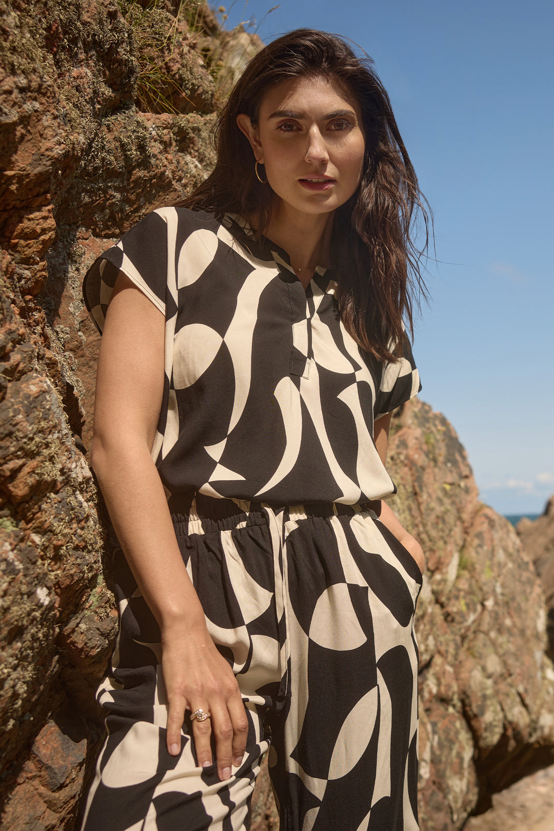 Woman in a black and white patterned split neck top standing against a rocky background