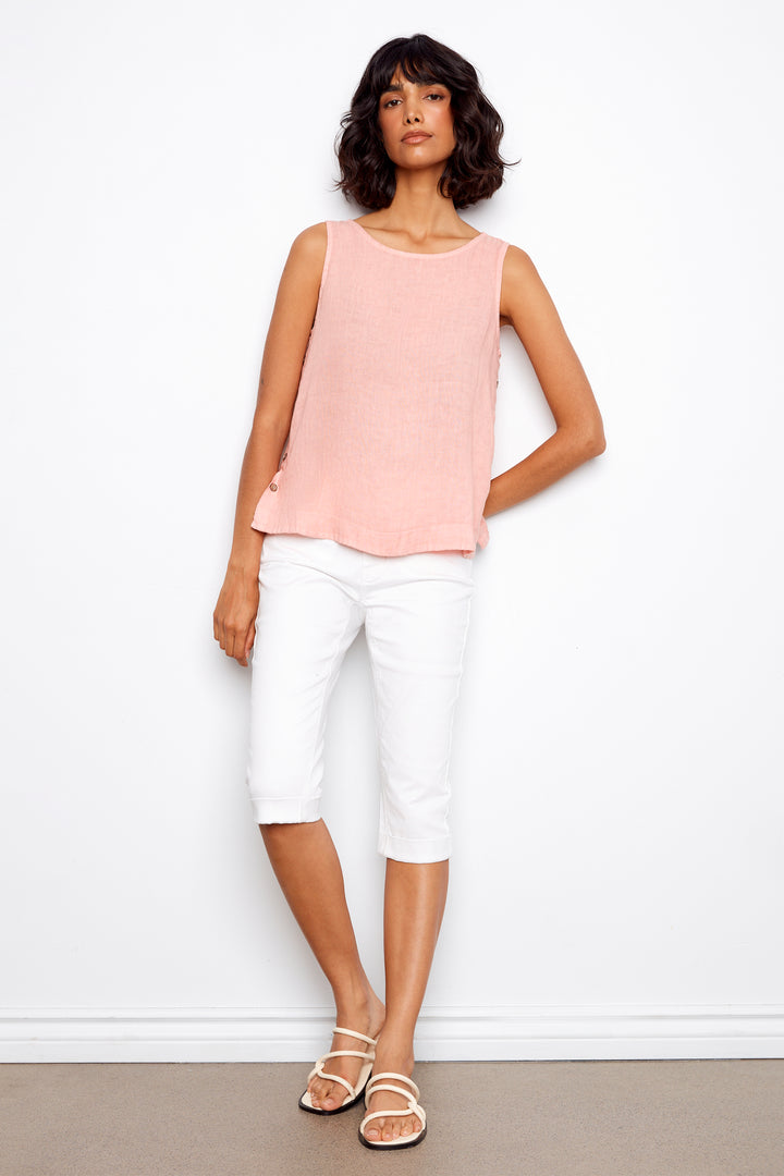 Woman wearing a pink sleeveless top and white pants against a plain background