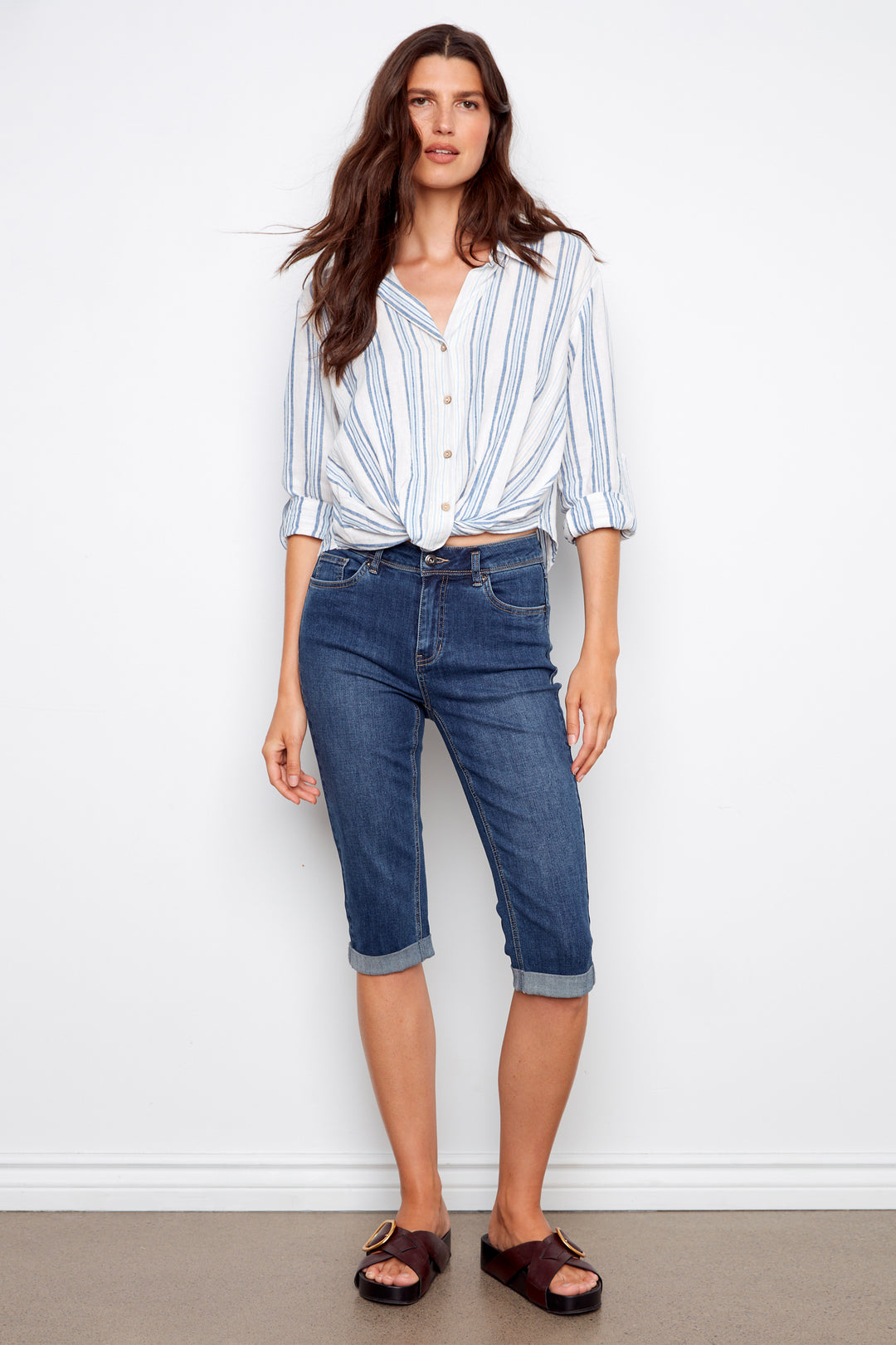 Woman wearing a striped shirt and blue jeans against a white background