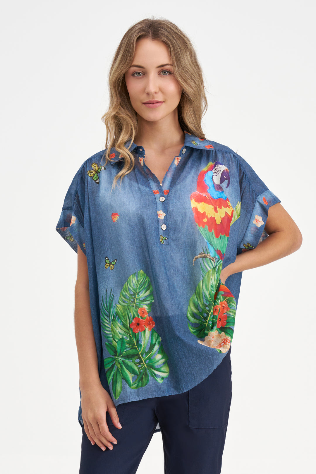 Woman wearing a blue denim shirt with tropical parrot and leaf designs on a white background