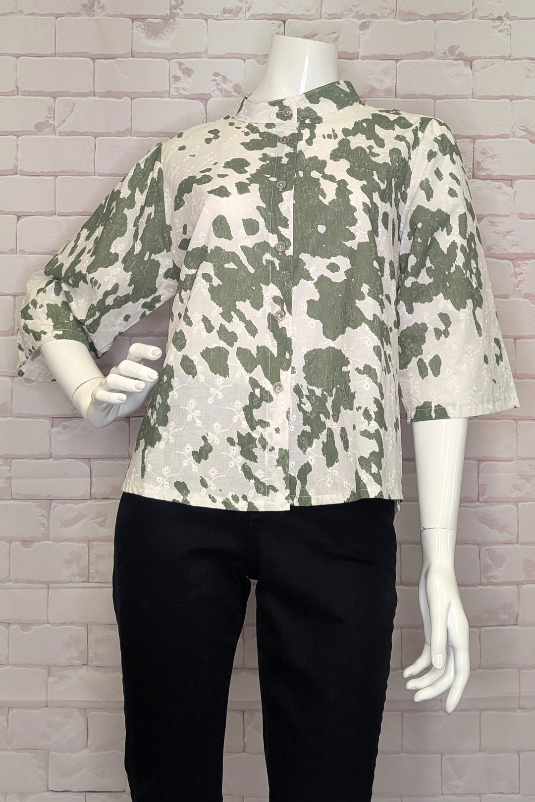 Mannequin wearing a camouflage-cactus patterned shirt against a gray brick wall.