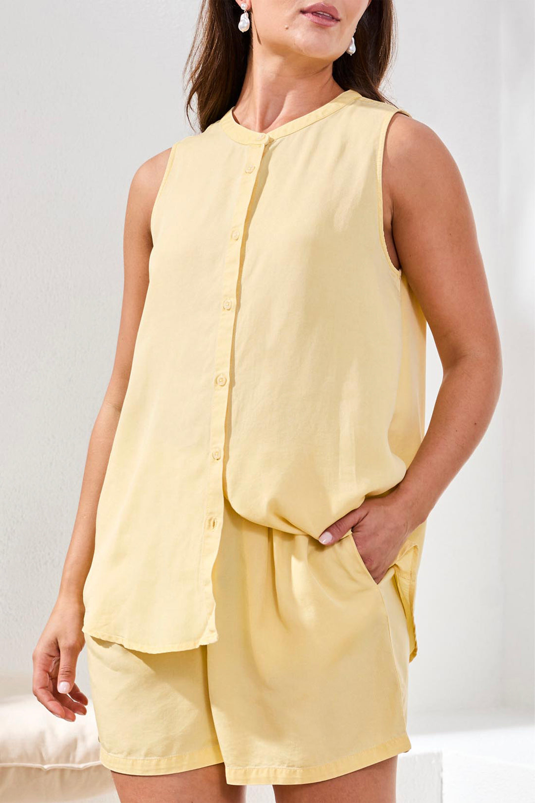 Woman wearing a yellow sleeveless top and shorts set against a white background
