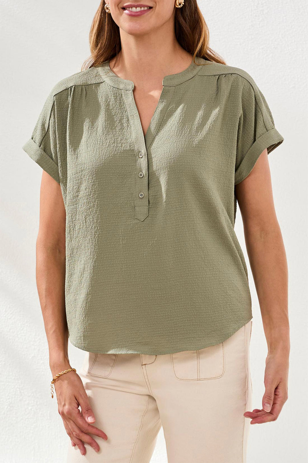 Woman wearing a green short-sleeve blouse with buttons and split neck with a plain background
