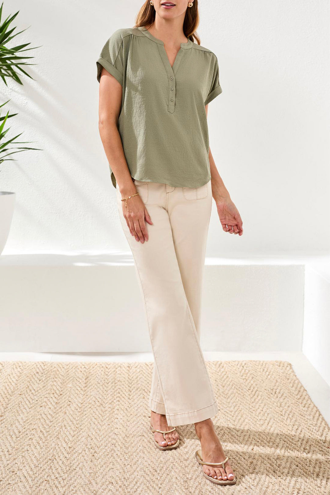 Woman wearing a green top and beige pants in a minimalistic setting