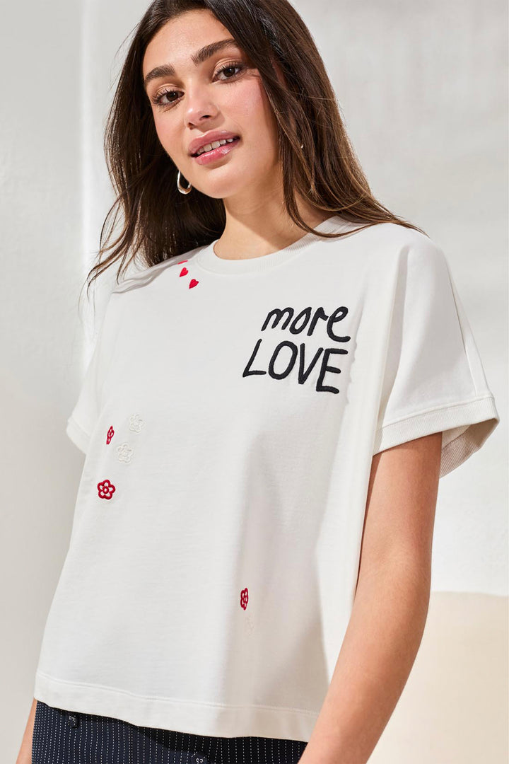 Woman wearing a white t-shirt with 'more love' text and small red graphics on a plain background