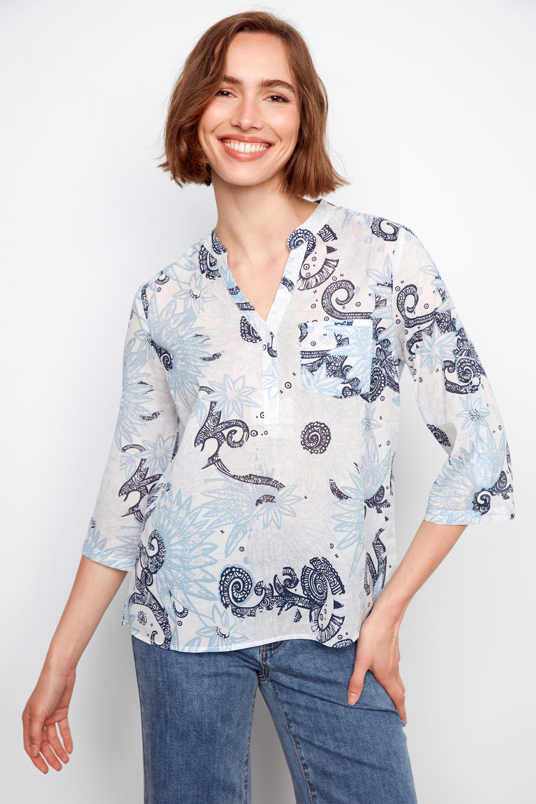 Woman wearing a white blouse with blue paisley patterns and blue jeans on a white background