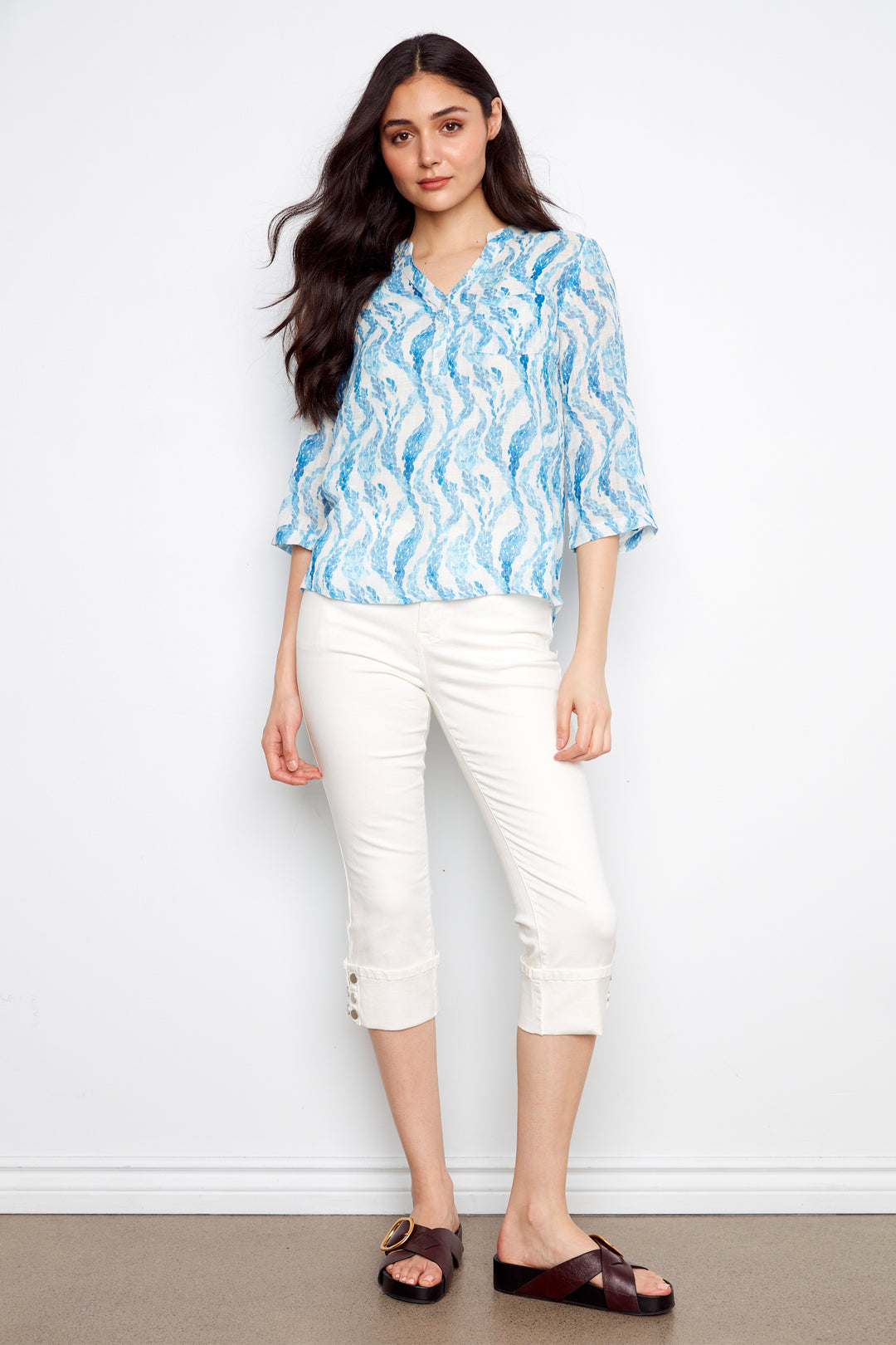 Woman wearing a blue patterned blouse and white pants against a white background