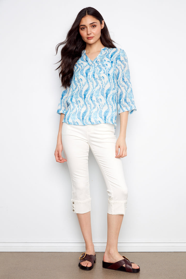 Woman wearing a blue patterned blouse and white pants against a white background