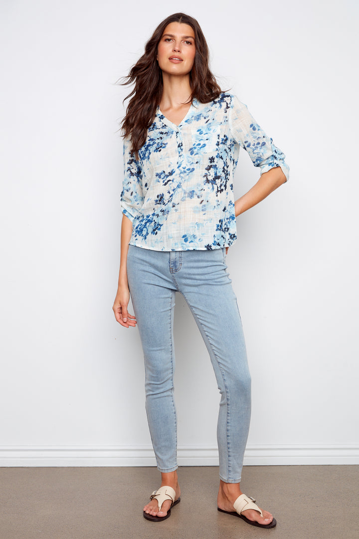 Woman wearing a floral blouse and light blue jeans against a white background
