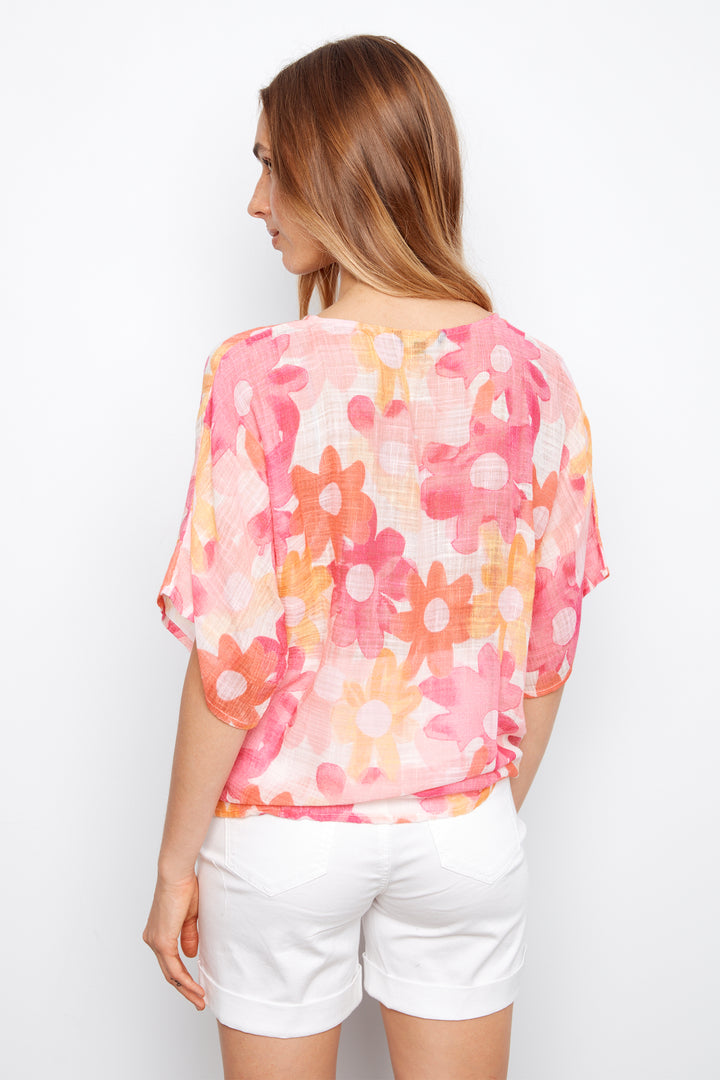 Woman wearing a floral blouse and white shorts on a plain background