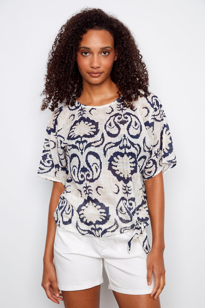 Woman wearing a patterned top and white shorts on a plain background