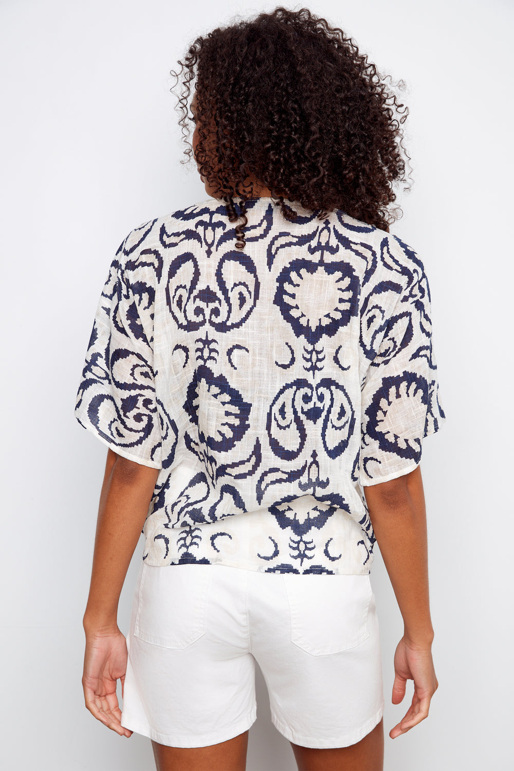 Person wearing a patterned top and white shorts on a plain background