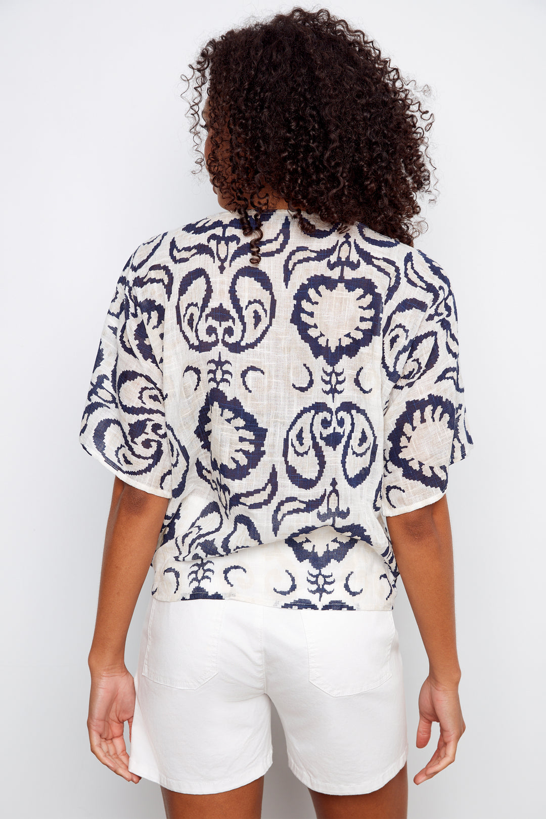 Person wearing a patterned top and white shorts on a plain background