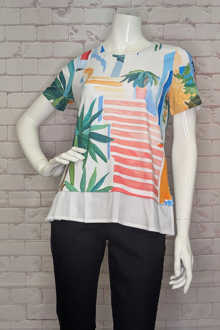 Mannequin wearing a colorful patterned top with a white base against a brick wall.