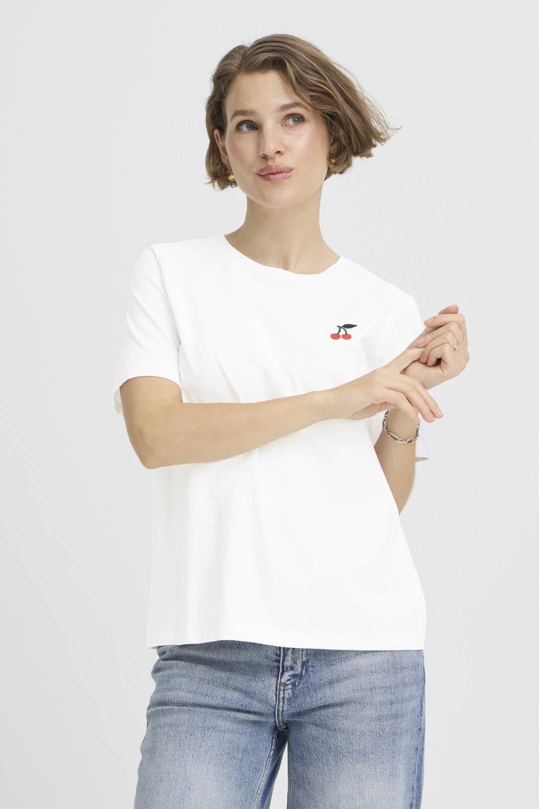 Woman wearing a white t-shirt with a small red logo on a plain background