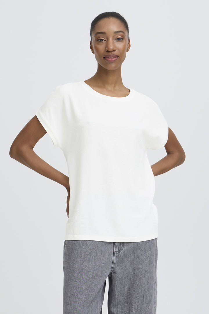 Woman wearing a white top and gray pants on a plain background